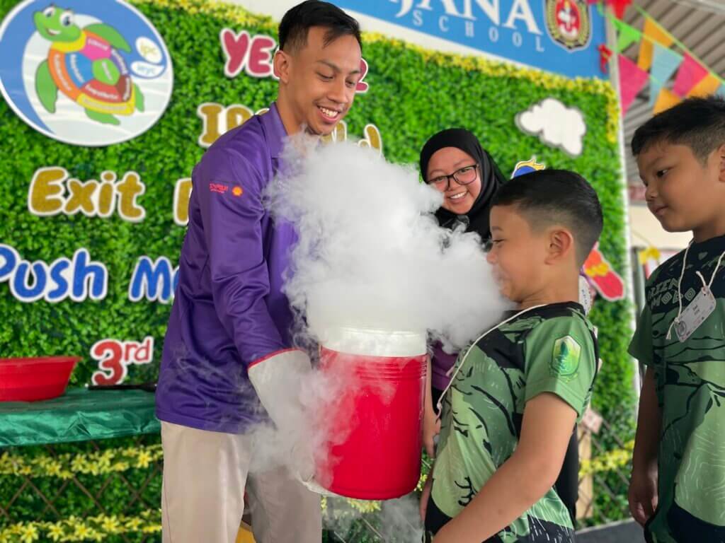 A man shows a young boy a science experiment with billowing white smoke at a school event.