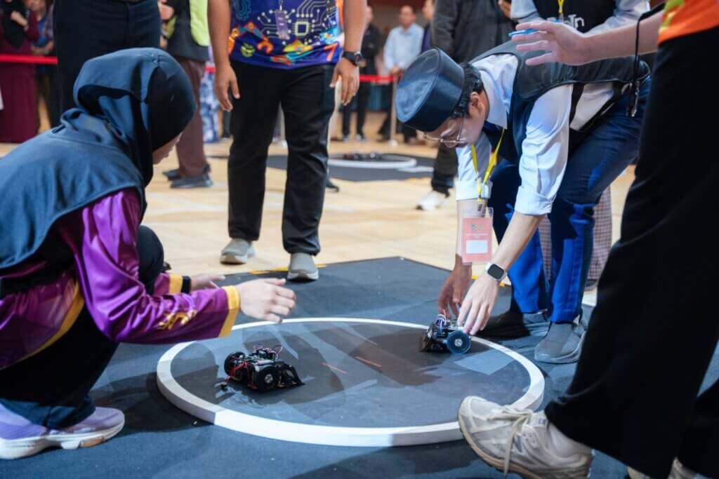 Students prepare robots for competition on a round, marked arena.