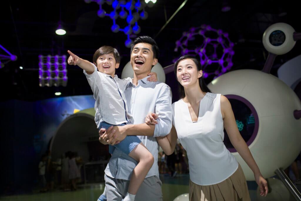 A young family enjoys a science museum exhibit, with the son pointing excitedly.