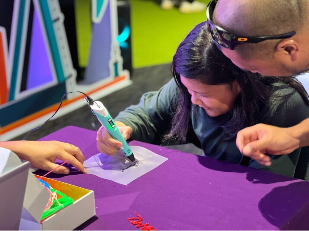 A young girl uses a 3D pen with assistance from an adult.