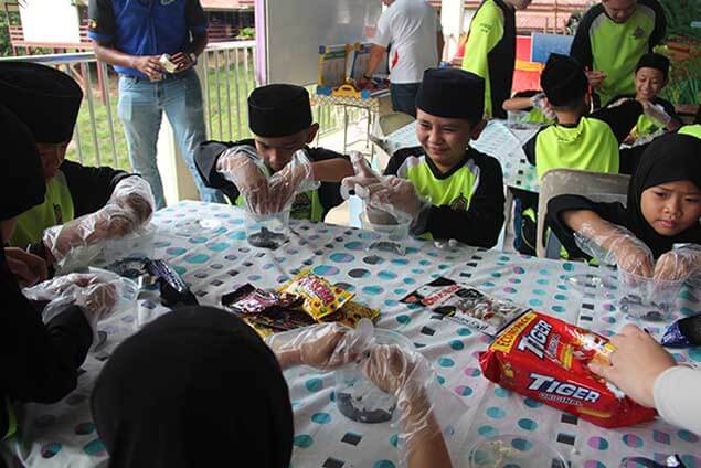 Children in gloves making something with snacks at a table.
