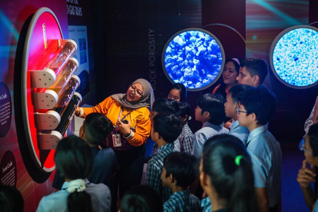 A woman explains oil and gas traps to a group of students at a science exhibit.
