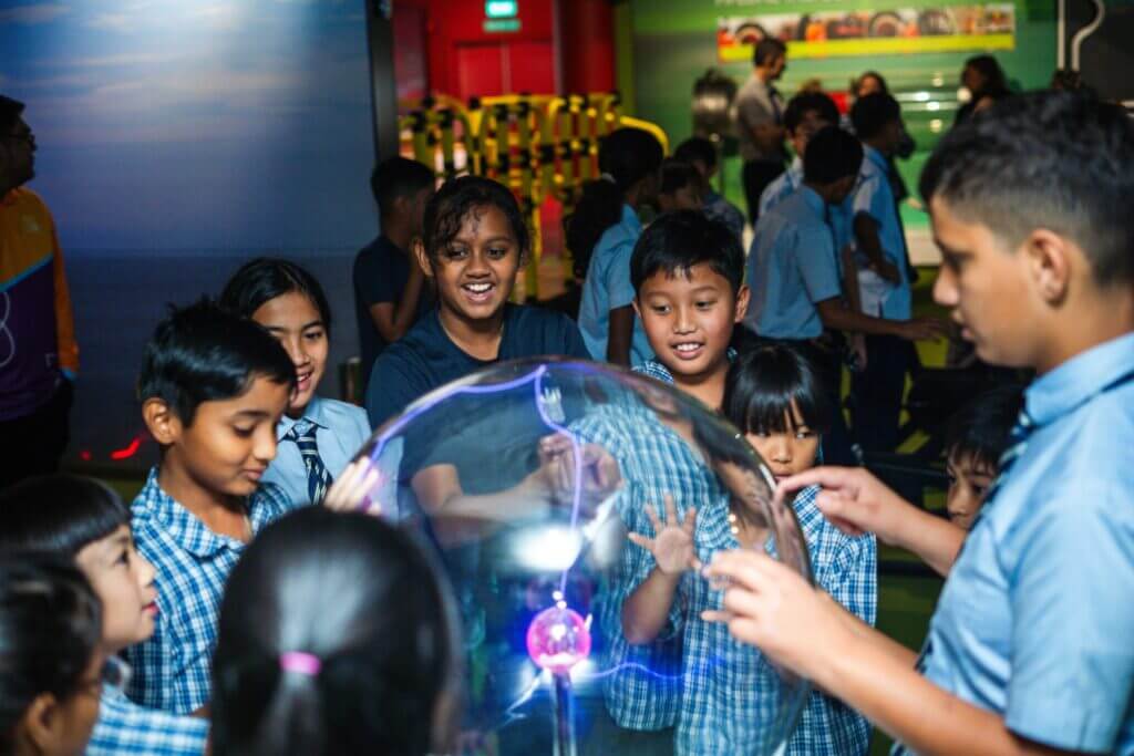 Children gathered around a plasma ball, smiling and interacting with the exhibit.