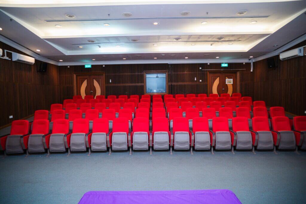 Auditorium with red seats and wood-paneled walls.