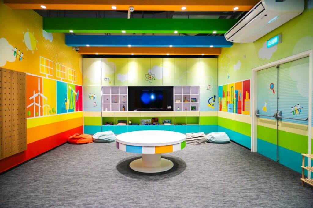 Brightly colored makerspace with a round table, beanbag chairs, and shelves filled with toys.