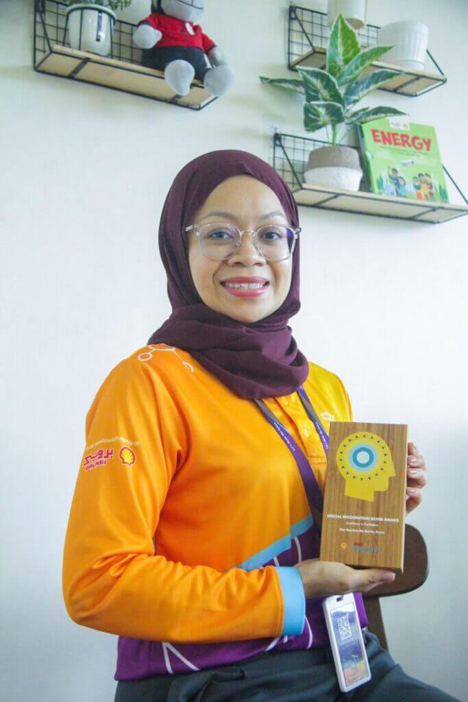 A woman in an orange shirt and hijab holds an NXPLORERS Recognition Silver Award.