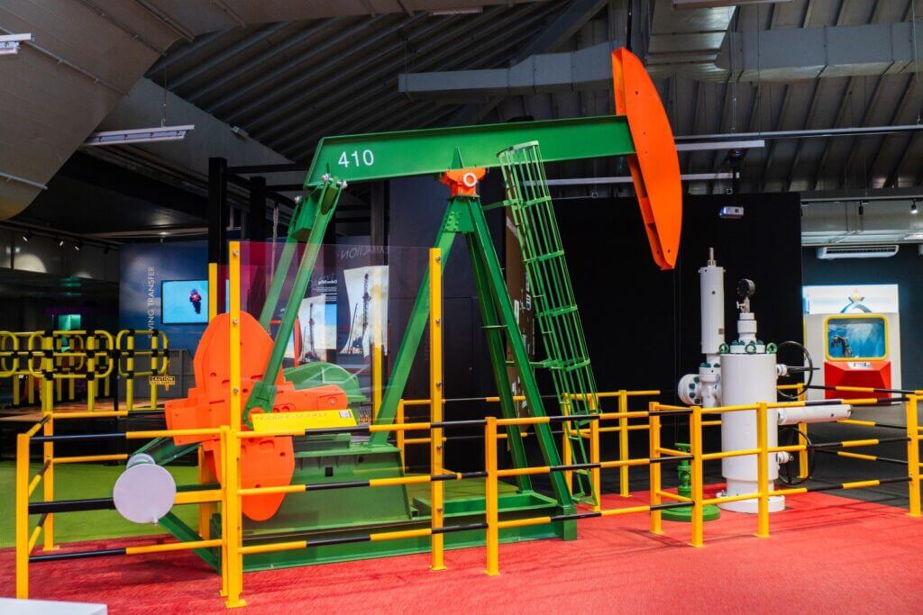 A colorful, fenced-off exhibit showcasing a model oil pumpjack and wellhead at "Oil and Gas Zone 4".
